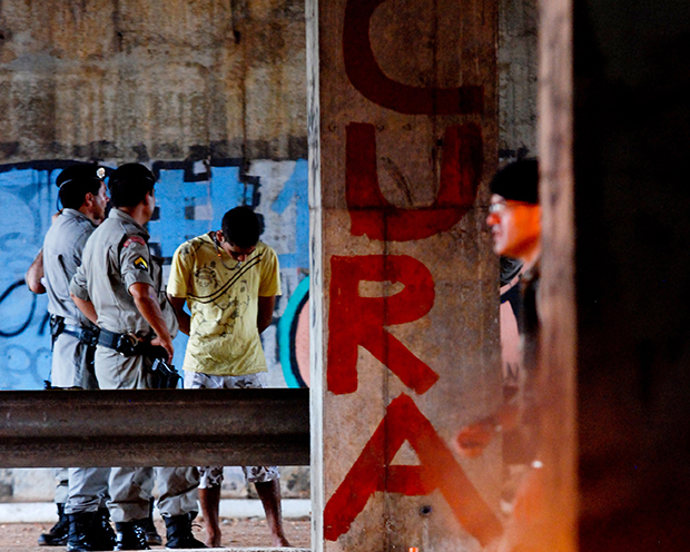 Jovem usuário de drogas algemado ao lado de uma pichação que diz aquilo que a grande parte dos dependentes procura: cura | Foto: Renan Accioly