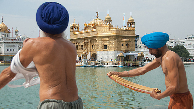 Homens torcem roupas após banho no lago do Templo de Ouro, em Amritsar