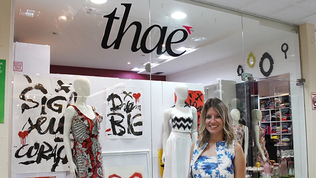 Thais Lemos na porta de sua loja, a Thaê, cuja vitrine segue a temática das coleções criadas pela estilista. Na foto, as peças da última, feita em parceria com artista de rua goiano | Foto: Bruna Aidar/ Jornal Opção